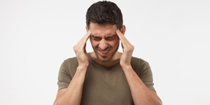 Portrait of young man isolated on grey background suffering from severe headache, pressing fingers to temples, closing eyes in order to relieve pain with helpless face expression